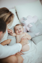 Smiling young couple playing with their beloved newborn baby girl on the bed