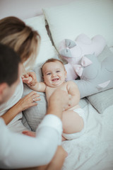 Smiling young couple playing with their beloved newborn baby girl on the bed