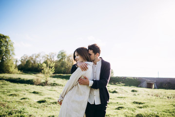 Lifestyle couple walking on grass in field on sunny day. Hug, kiss, hold hands, have fun. Warm photo with lens flare