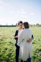 Lifestyle couple walking on grass in field on sunny day. Hug, kiss, hold hands, have fun. Warm photo with lens flare