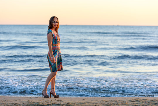 Bella donna ritratto sulla spiaggia con abito multicolore estivo e tacchi alti