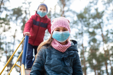 European children playing on the playground outdoor during epidemic of dangerous virus. Small children wearing medical masks for protection