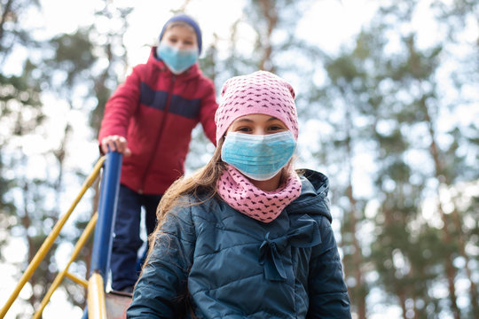 European Children Playing On The Playground Outdoor During Epidemic Of Dangerous Virus. Small Children Wearing Medical Masks For Protection