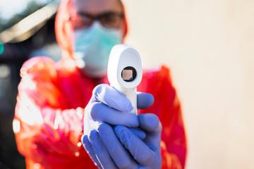 Man in protective suit, gloves and mask, controlling body temperature with infrared forehead...