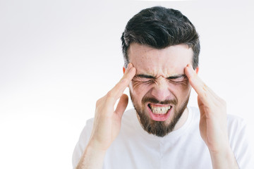 Picture of young bearded brunette man suffer from strong pain or headache. Hold fingers close to side of head. Need pill or medicine for relief. Isolated over background.