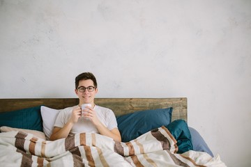 This is wonderful morning. A young man waking up in bed . man in bed drinking morning coffee in sunrise light