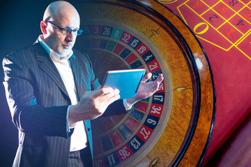 An astonished man with a tablet in his hands on the background of a roulette wheel. Losing in an...