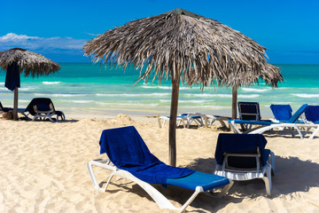 Vacation in Cuba. Beach on the Caribbean sea. Sun beds and umbrellas made of palm leaves on the...