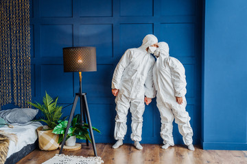 Stay safe! Young couple of doctors standing near the wall and kissing wearing a face mask protection against coronavirus. People in protective suits stay at home isolated due to epidemic of covid-19