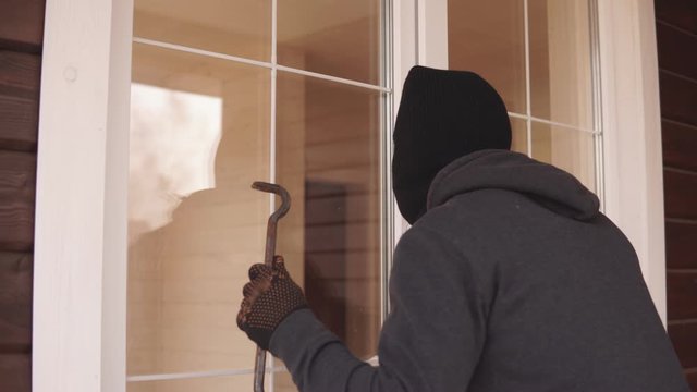 A burglar with crowbar trying to get into a house by the backdoor. Thief looking through the closed door inside house