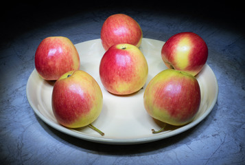 Ripe apples on a round plate. Red and yellow juicy apples. Still life with apples.