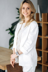Formal portrait of a beautiful attractive blonde girl in stylish white suit and with charming smile. Indoors