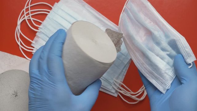 Doctor showing rolls toilet paper and antiviral face masks on red background. Human hands protected blue medical gloves. Lavatory paper, protection masks - concept fight against coronavirus, hygienics