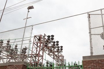 Electric power plant structures with insulators and trusses behind brick and chain link wall,...