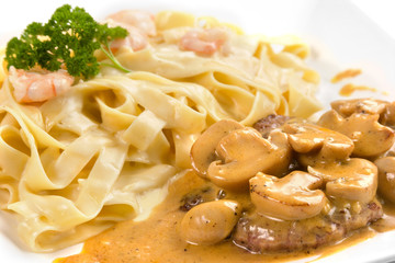 Closeup of fetucinni with shrimps sauce and beef steak with mushrooms serve on a white plate
