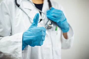 Closeup of a woman doctor wearing white medical gown and blue gloves, stethoscope. Female nurse holding stethoscope and showing thumb up like. Coronavirus, covid-19 and sickness prevention concept.