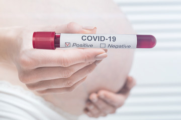 Pregnant woman holding biological tube with positive result on COVID-19. Coronavirus during...