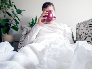 Sick man drinking from red Cup lying on the couch during the quarantine, cold, virus or flu