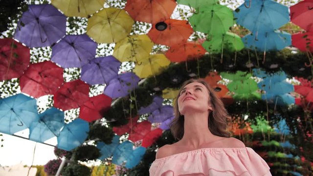 A girl walks on the background of multi-colored umbrellas in a park in the city