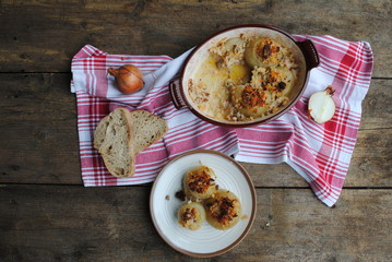 Stuffed Onions in Ceramic Baking Dish and plate, on a wooden rustic background. Top view.