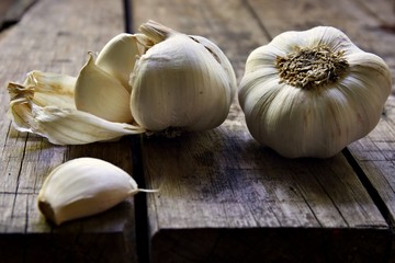 Isolated whole cloves of garlic with one whole clove having been opened and a clove taken out and placed in the foreground.  The garlic sits on the edge of a wooden table.