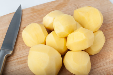  peeled potatoes lies on a kitchen wooden cutting board. isolate on white background
