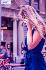 Fototapeta premium Young Eastern European American Woman talking on cell phone, traveling, working in New York City, wearing blue dress, carrying laptop computer, walking on street in Manhattan. Color filtered effect..