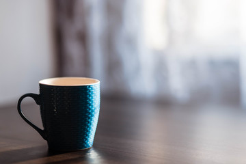 Cup. Blue cup standing on a wooden table. Blurred background. The sun is shining on the cup.