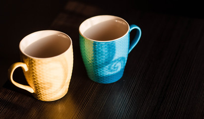 Cups. Colored cup standing on wooden table. Blurred background. The sun is shining on the cup.