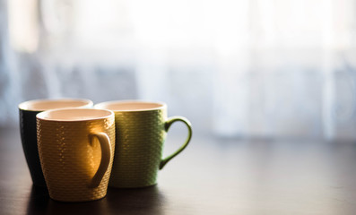 Cups. Colored cup standing on wooden table. Blurred background. The sun is shining on the cup.