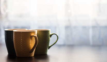 Cups. Colored cup standing on wooden table. Blurred background. The sun is shining on the cup.