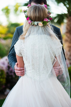 Scene of the back of a bride with a flower crown and grooms gentle embrace