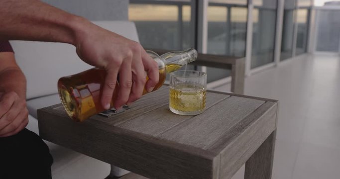 Man Pouring whiskey drink on balcony