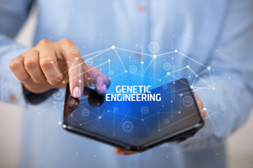 Businessman holding a foldable smartphone with GENETIC ENGINEERING inscription, new technology concept