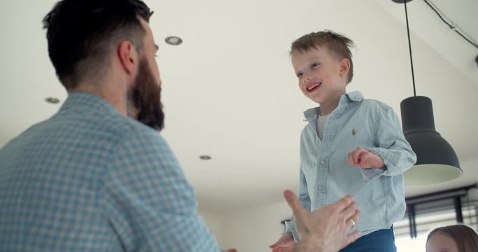 Cheerful happy cute little boy having fun shouting, jumping into young father arms at home, family time slow motion.