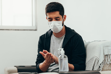 Coronavirus. Man in quarantine wearing protective mask sanitizing his hands with alcohol gel