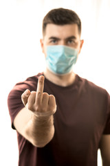 Theme of coronavirus and safety. A young man in a blue virus mask shows his middle finger. Vertical frame