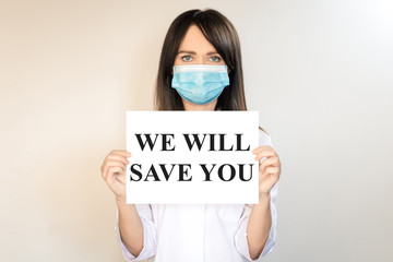 The topic of coronavirus and safety. A young female doctor with dark hair in a mask from a virus holds a white sheet with the inscription "We will save you." Horizontal frame