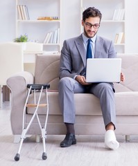 Businessman with crutches and broken leg at home working