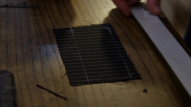 Man Tailor or clothing designer marking out pattern for a handmade garment on a length of black textile measuring to ensure a perfect fit for his client