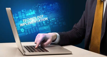 Businessman working on laptop with TECHNOLOGY IMPLEMENTATION inscription, cyber technology concept
