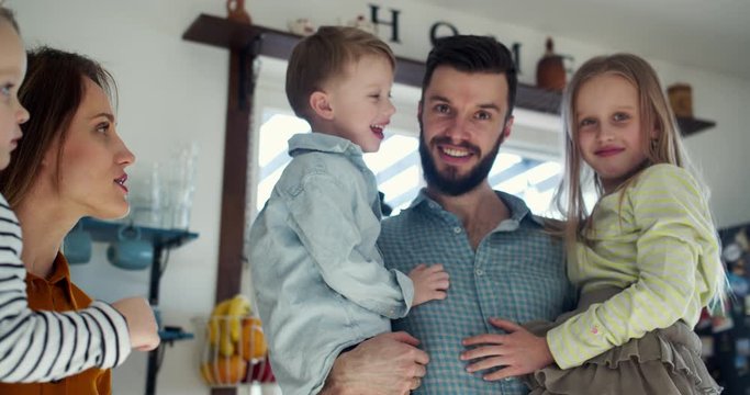 Family portrait, happy young Caucasian mother and father looking at camera holding three children at home slow motion.