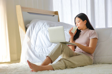 Young pretty girl working from home on her bed using computer laptop to access her work online...