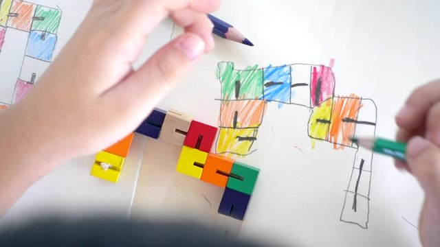 Top view & Closeup, Hands of kindergarten kid copy shapes of colorful wooden block, draw and color on plain notebook, to improve hand eye coordination, fine motor skills, muscular, brain development