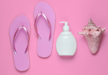 Beach accessories. Fashionable beach pink flip flops, sunblock bottle, seashell on pink paper...