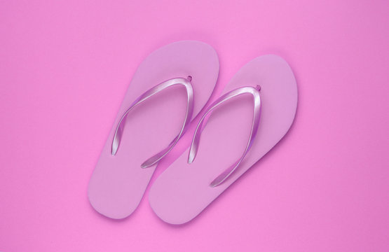 Trendy beach pink flip flops on pink paper background. Top view