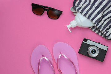 Summer still life. Beach accessories. Fashionable pink flip flops, bag, retro camera, sunblock bottle, sunglasses on pink paper background. Flat lay. Copy space. Top view