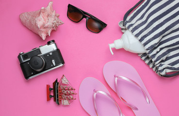 Obraz na płótnie Canvas Summer still life. Beach accessories. Fashionable pink flip flops, bag, retro camera, sunblock bottle, sunglasses, seashell on pink paper background. Flat lay. Copy space. Top view