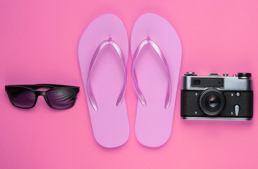 Summer still life. Beach accessories. Fashionable pink flip flops, bag, retro camera, sunglasses, ship on pink background. Flat lay. Top view