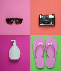 Summer still life. Beach accessories. Fashionable pink flip flops, retro camera, sunblock bottle,...